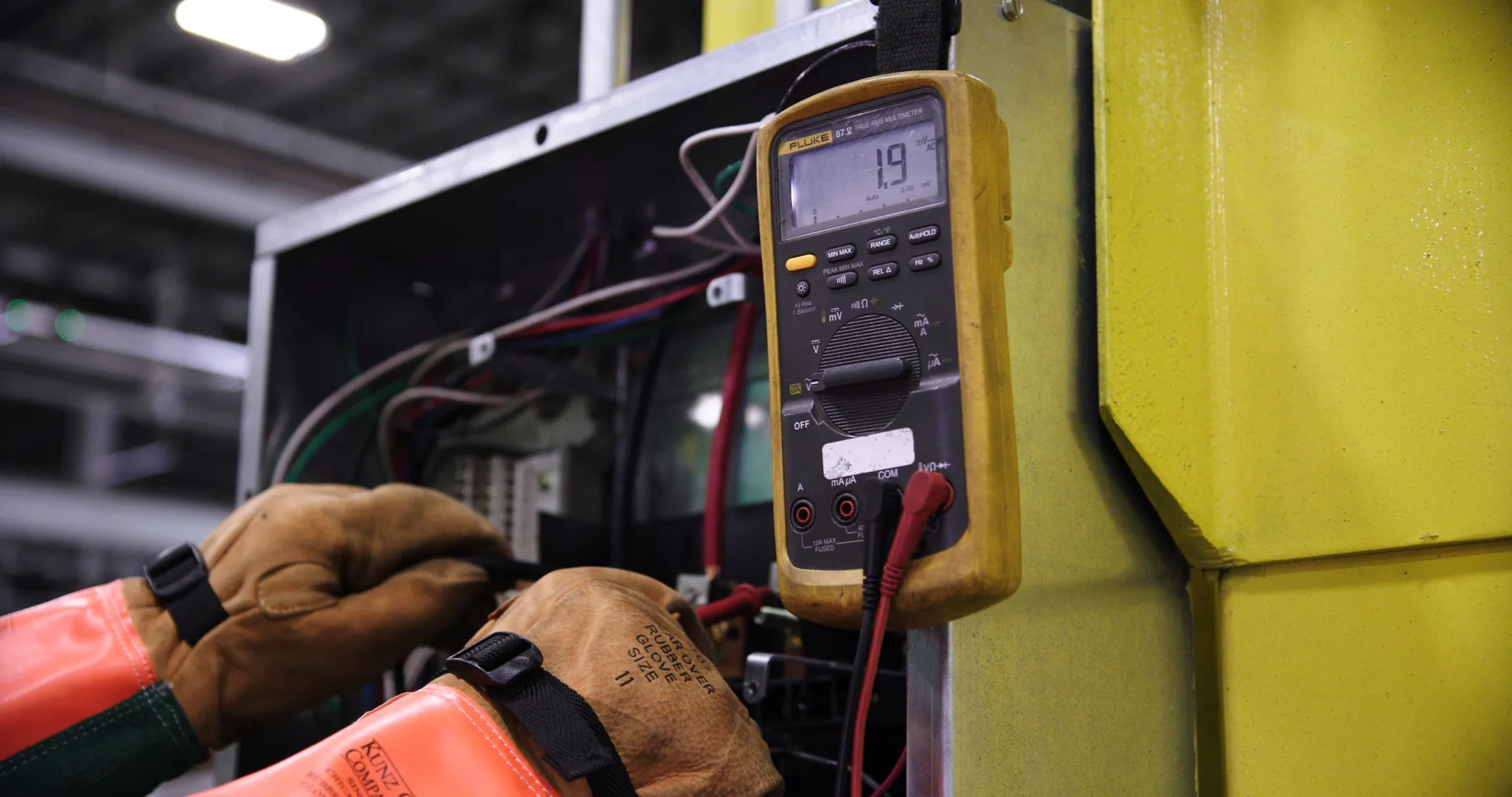A worker using a multimeter on an open electrical panel