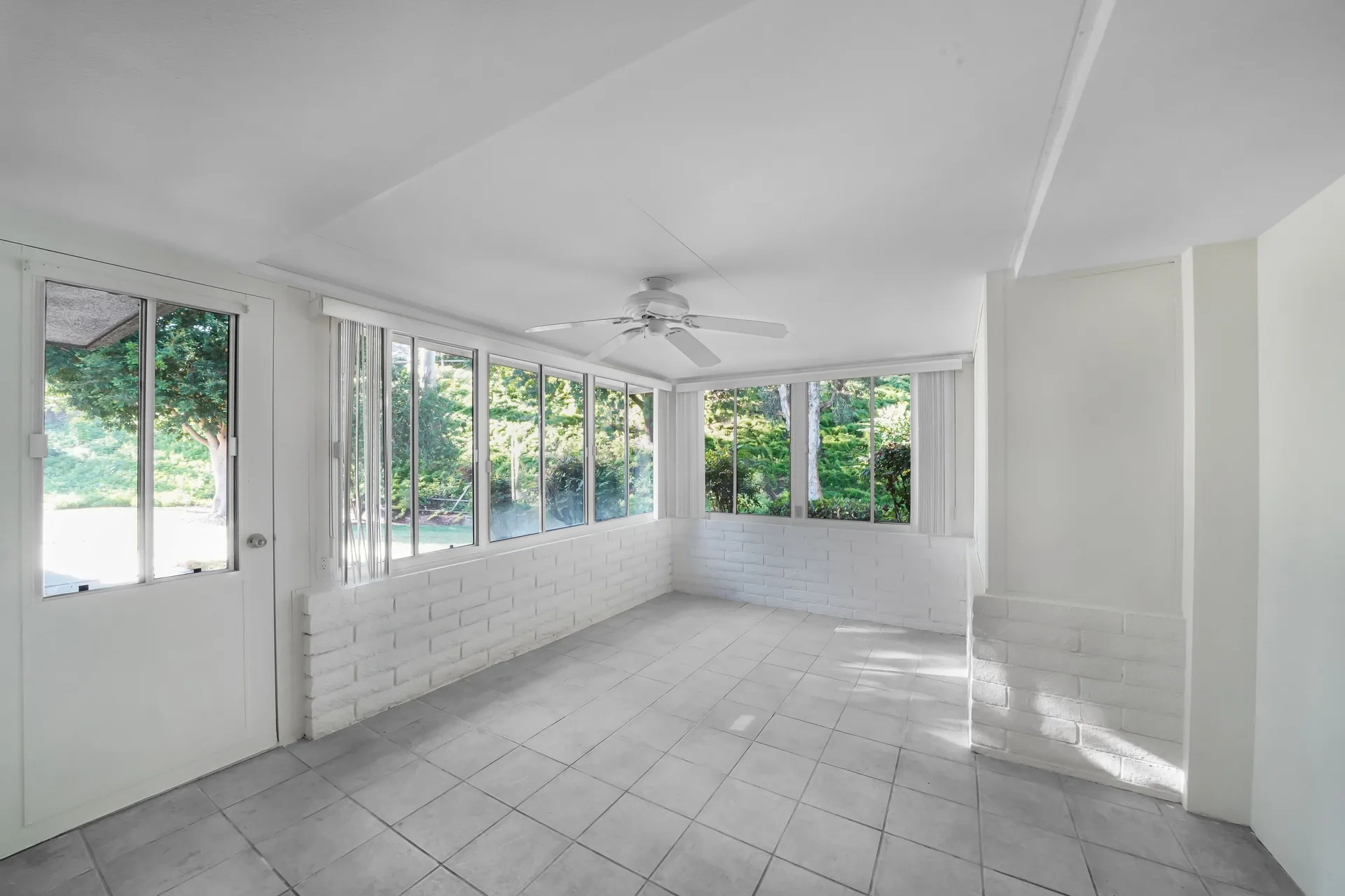 A ceiling fan in a bright sunroom with large windows
