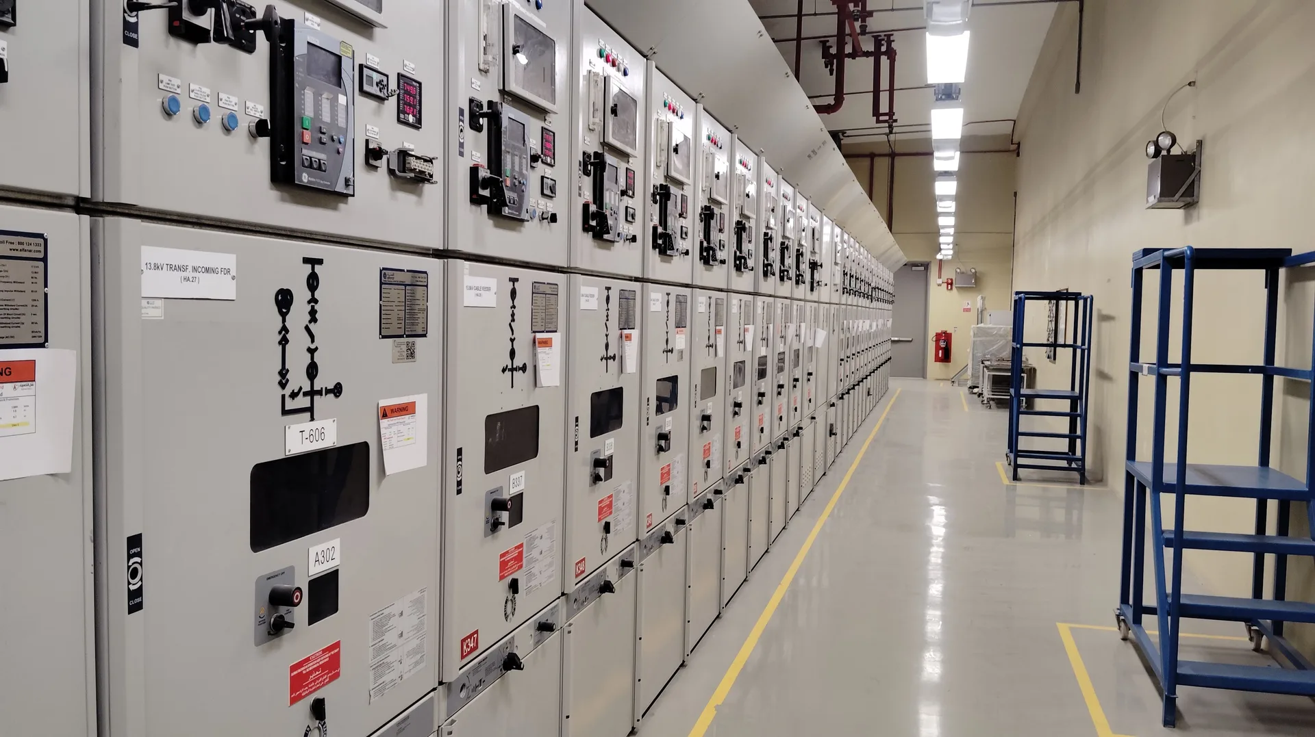 A long row of control panels in a well-lit industrial electrical control room