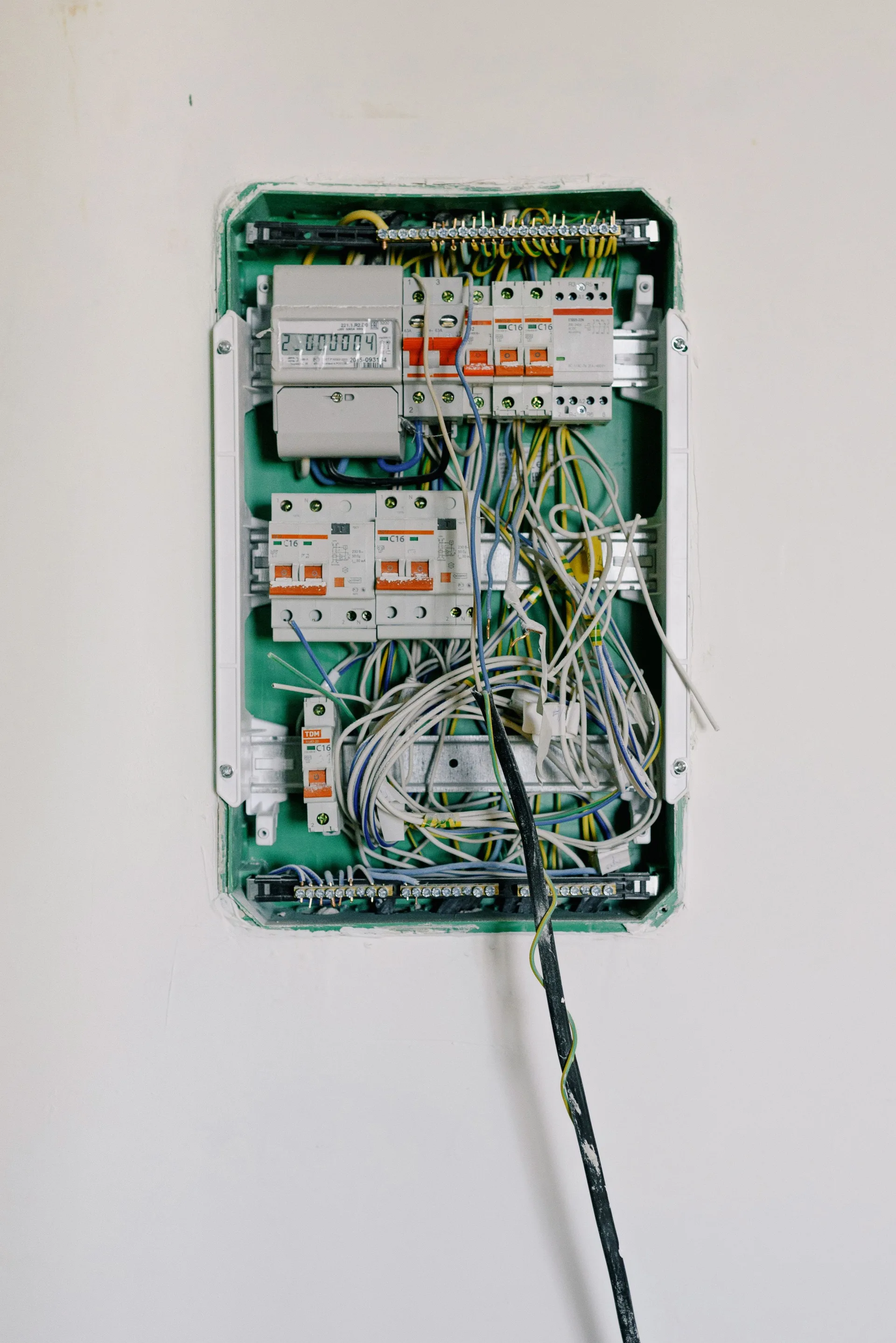 An open switchboard with wires connected to circuit breakers on a white wall