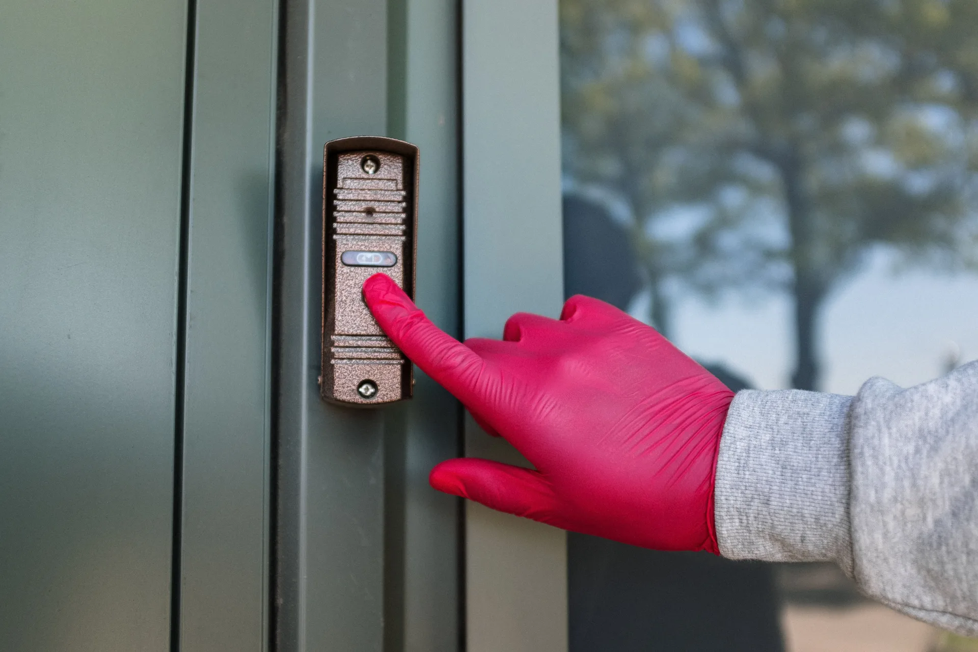A gloved hand pressing a modern doorbell button on a metal door