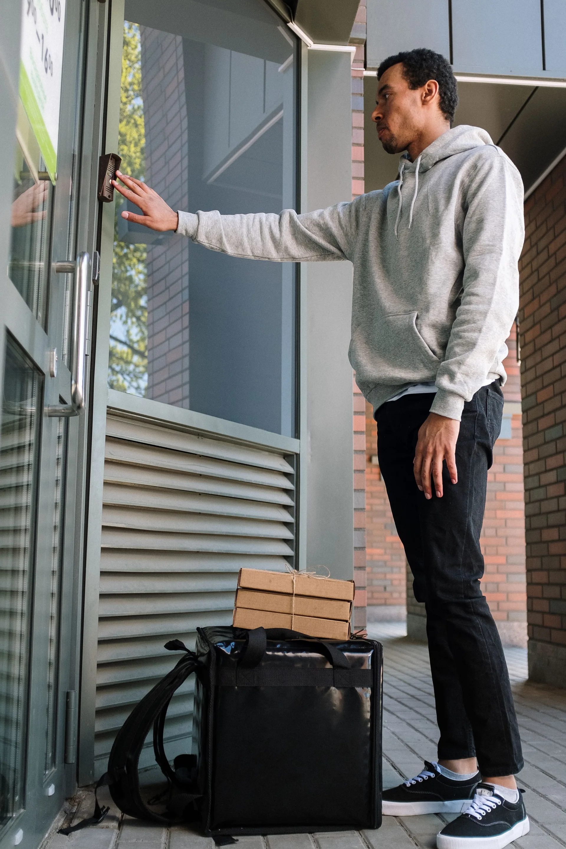 A courier ringing a doorbell at a modern building entrance