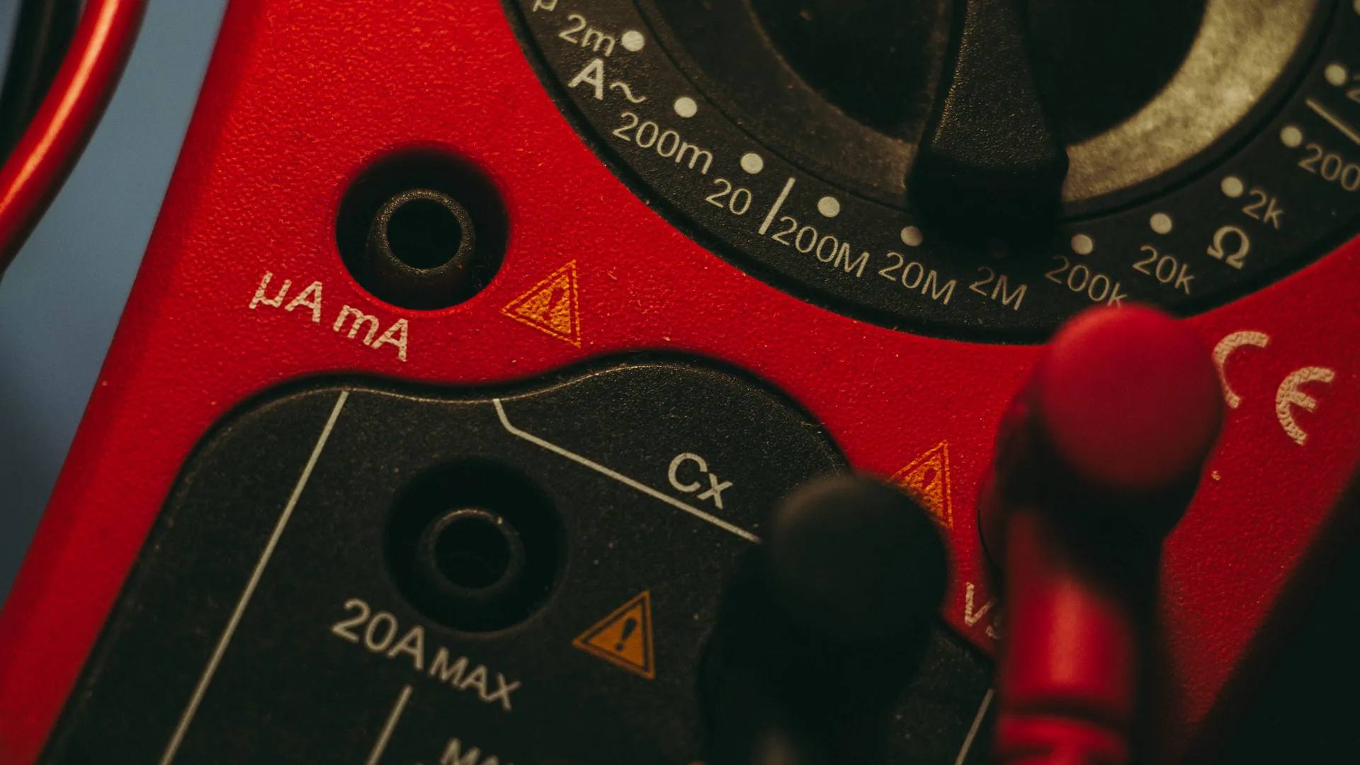 A red handheld meter with a measurement dial and test leads