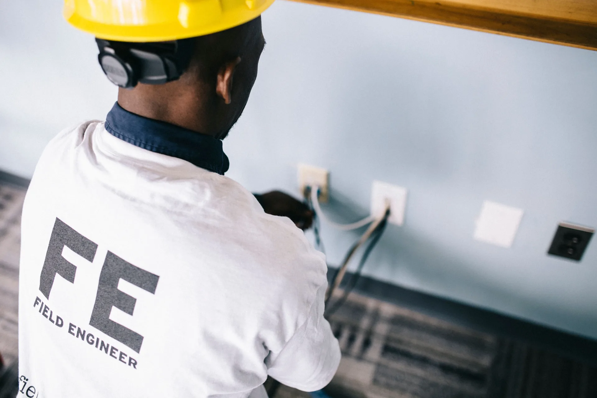 An engineer in a hard hat checking voltage at wall outlets indoors
