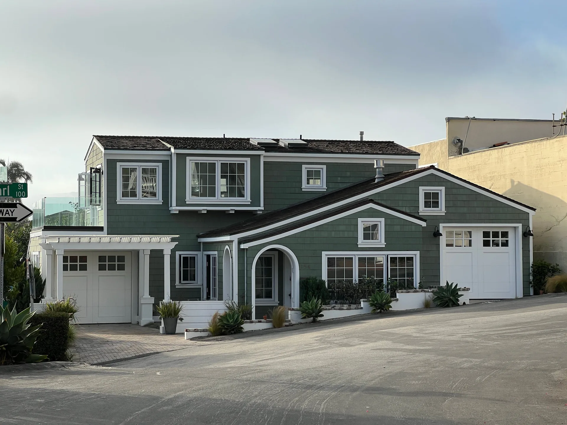 A green two-story suburban house with white trim and garages on a street corner