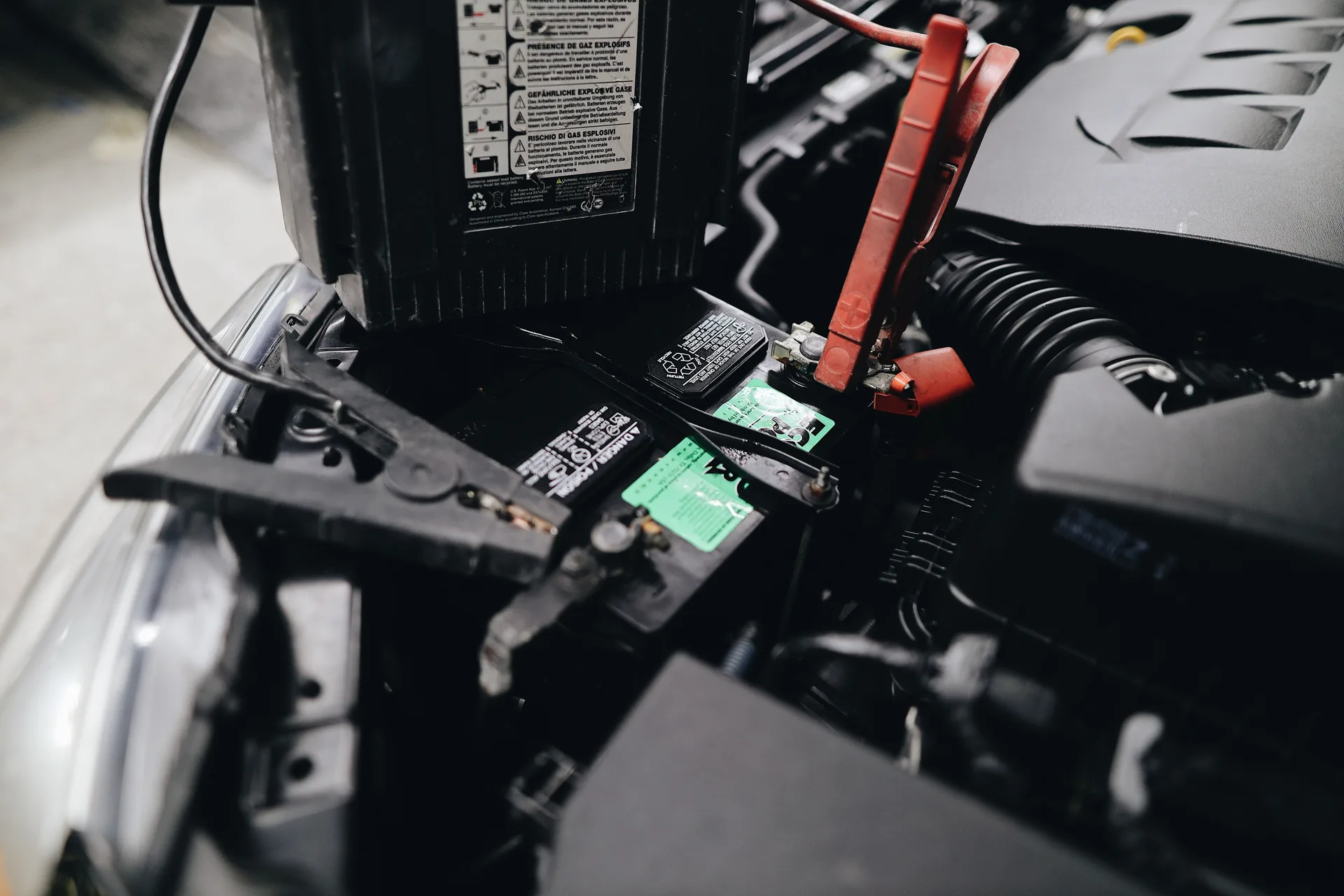 Car battery with jumper cables connected in an engine bay