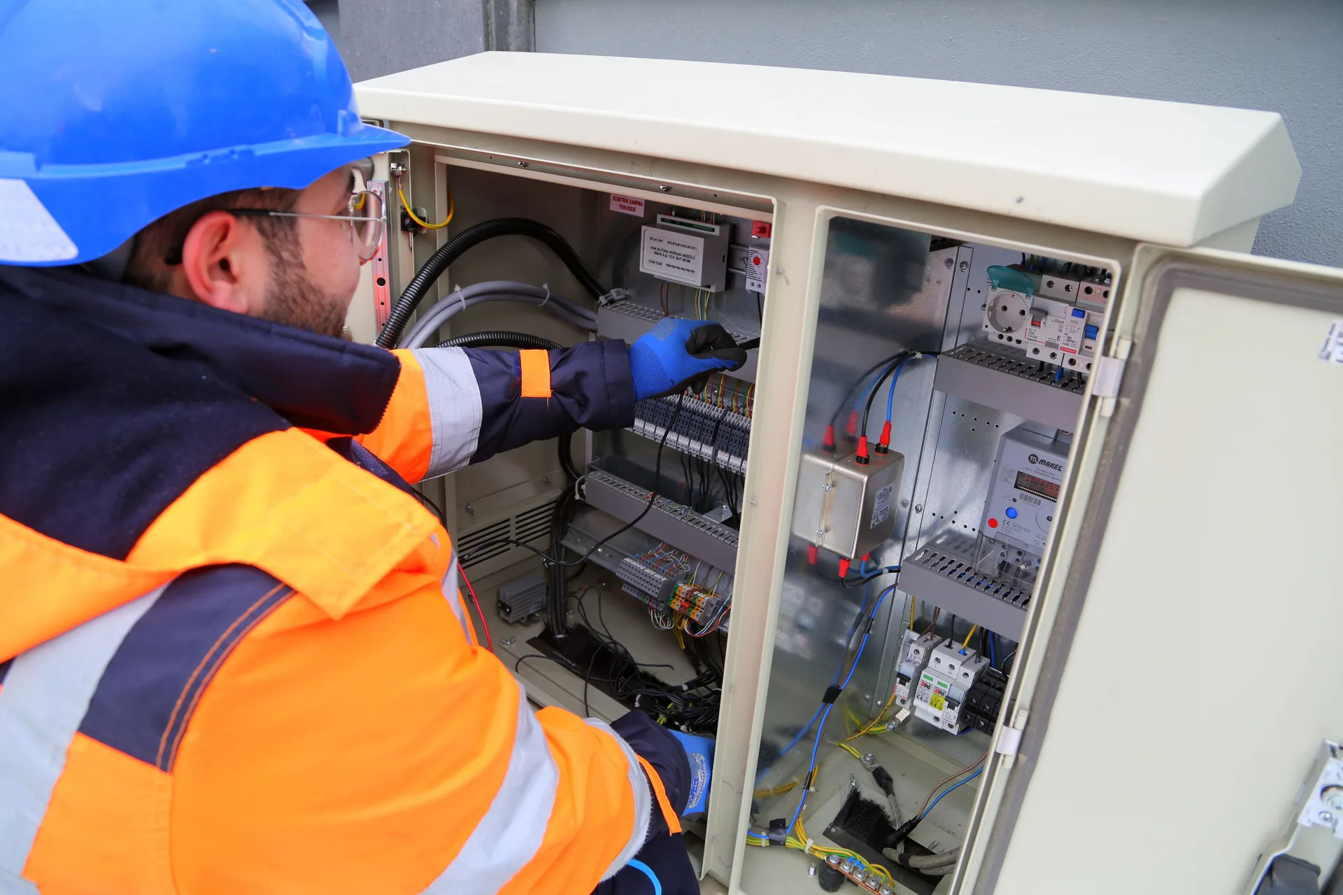 An engineer in safety gear working on an outdoor electrical panel