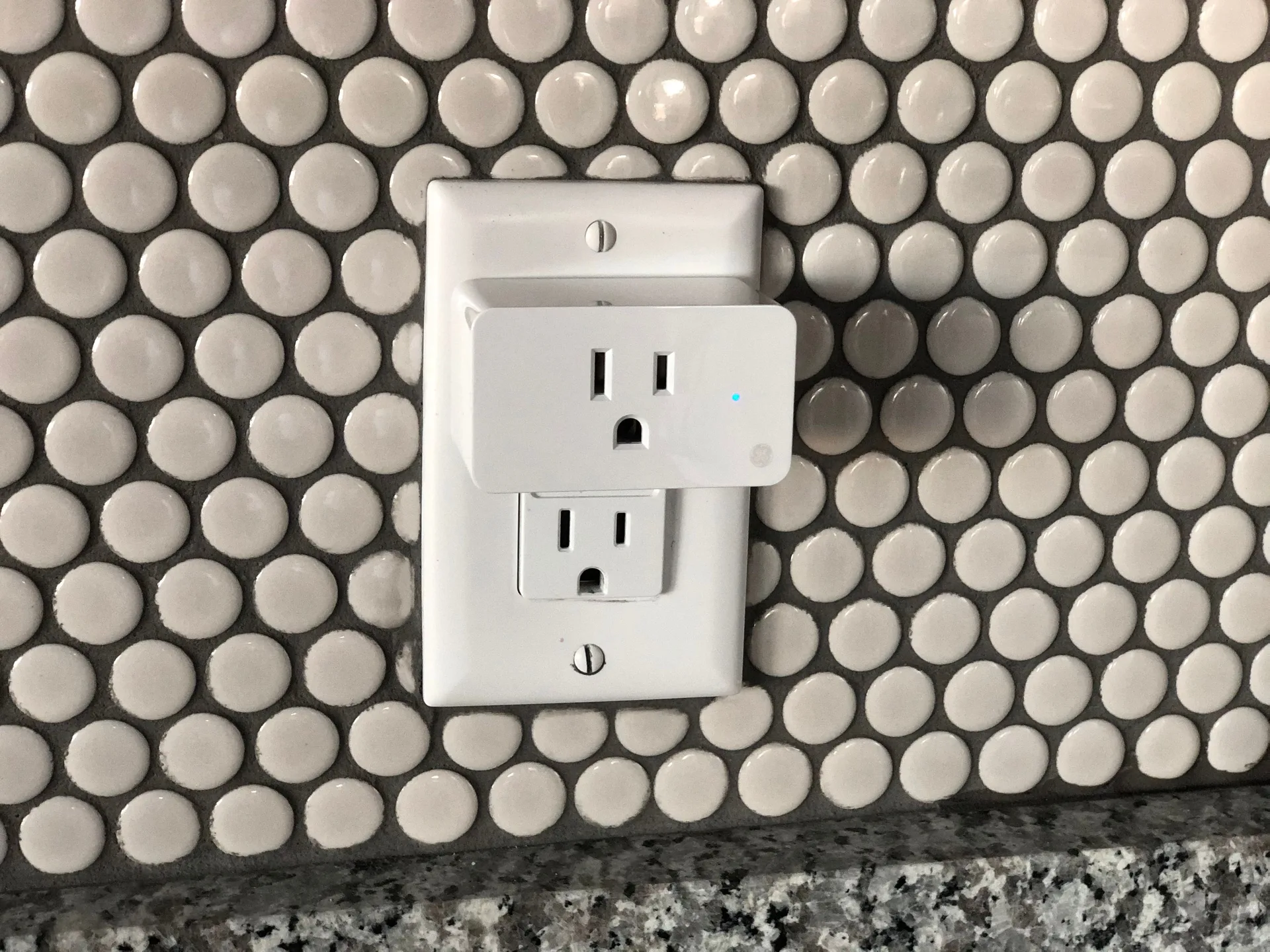A smart plug fitted in an outlet on a tiled wall