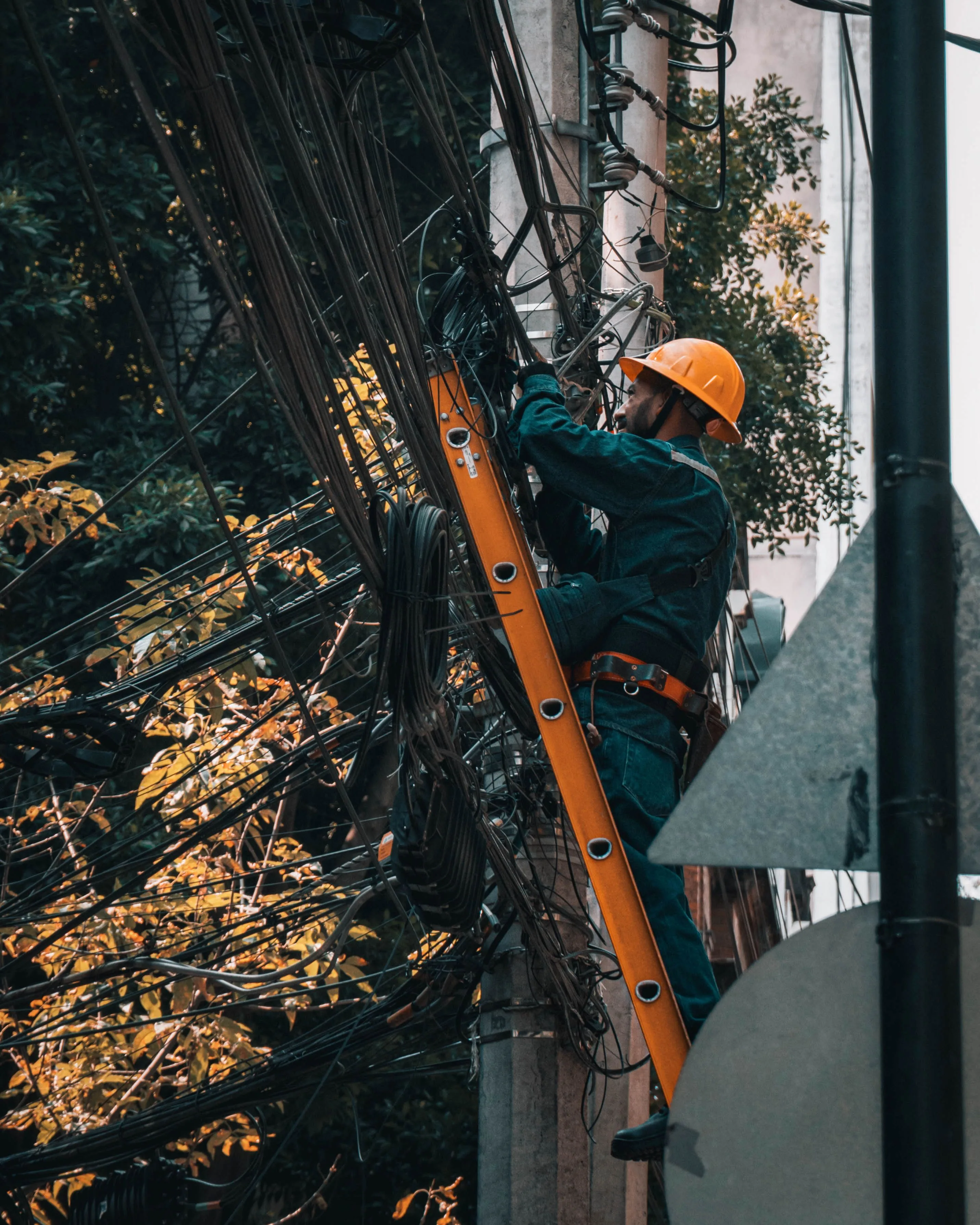 An electrician on a ladder working on overhead power lines outdoors