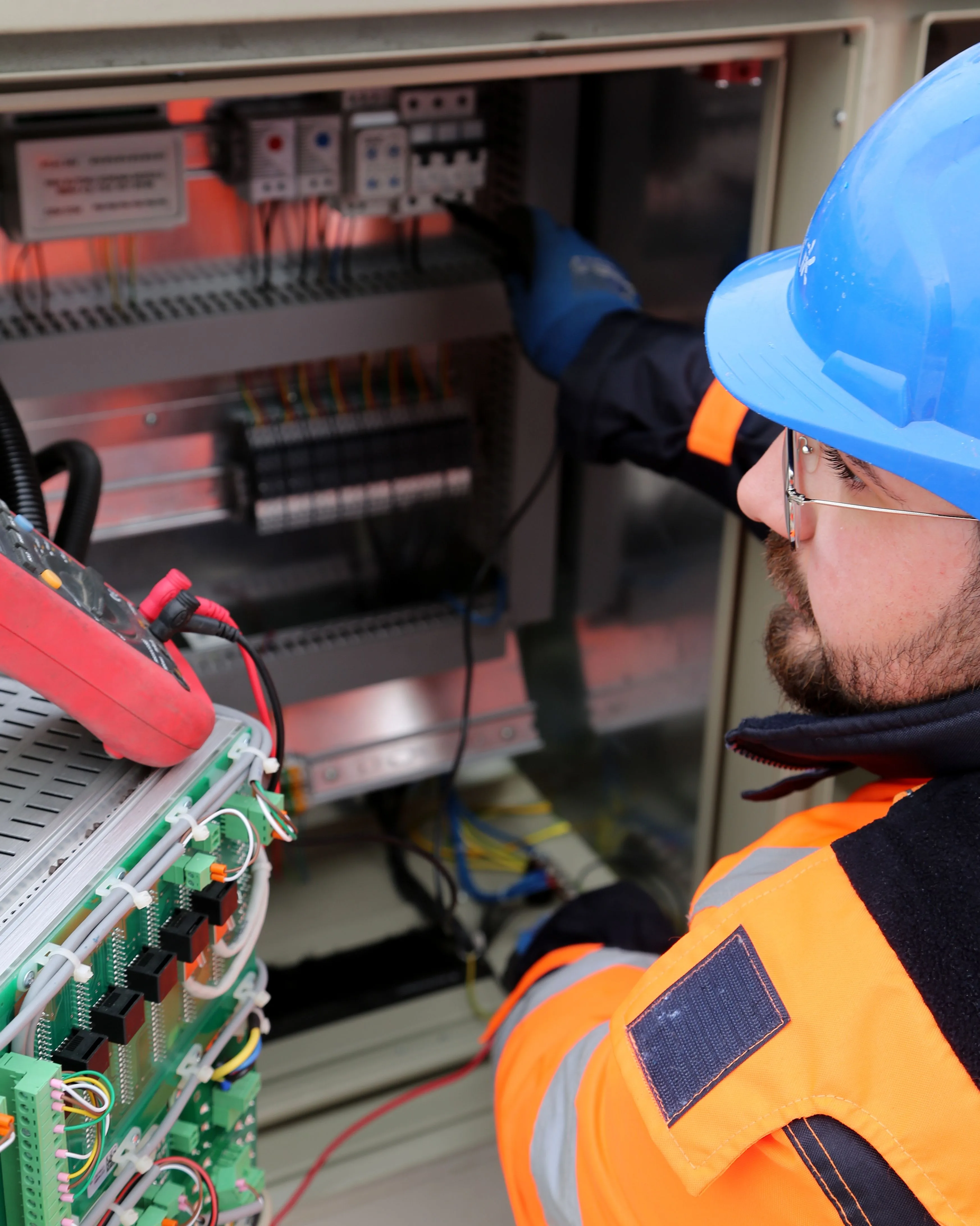 An electrician in safety gear working on an electrical switchboard