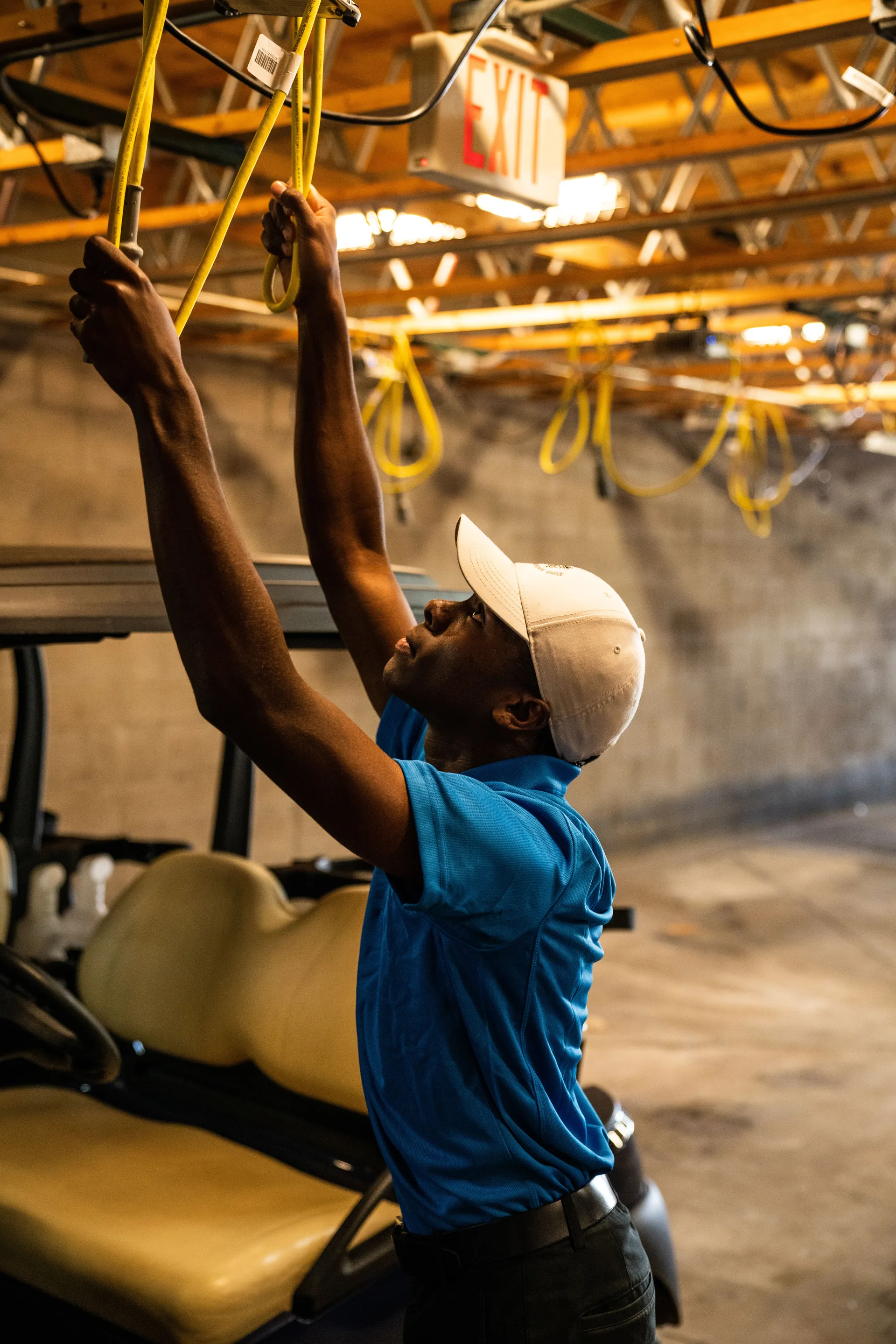 A worker in a cap working on wiring above a vehicle in a garage