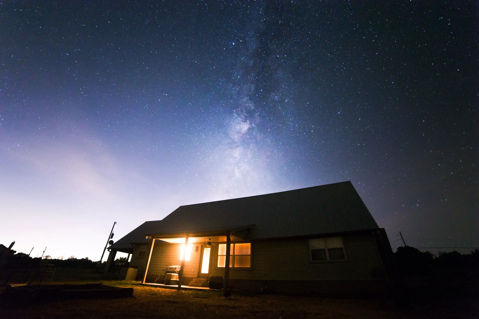 House lit at night under a starry sky with the Milky Way