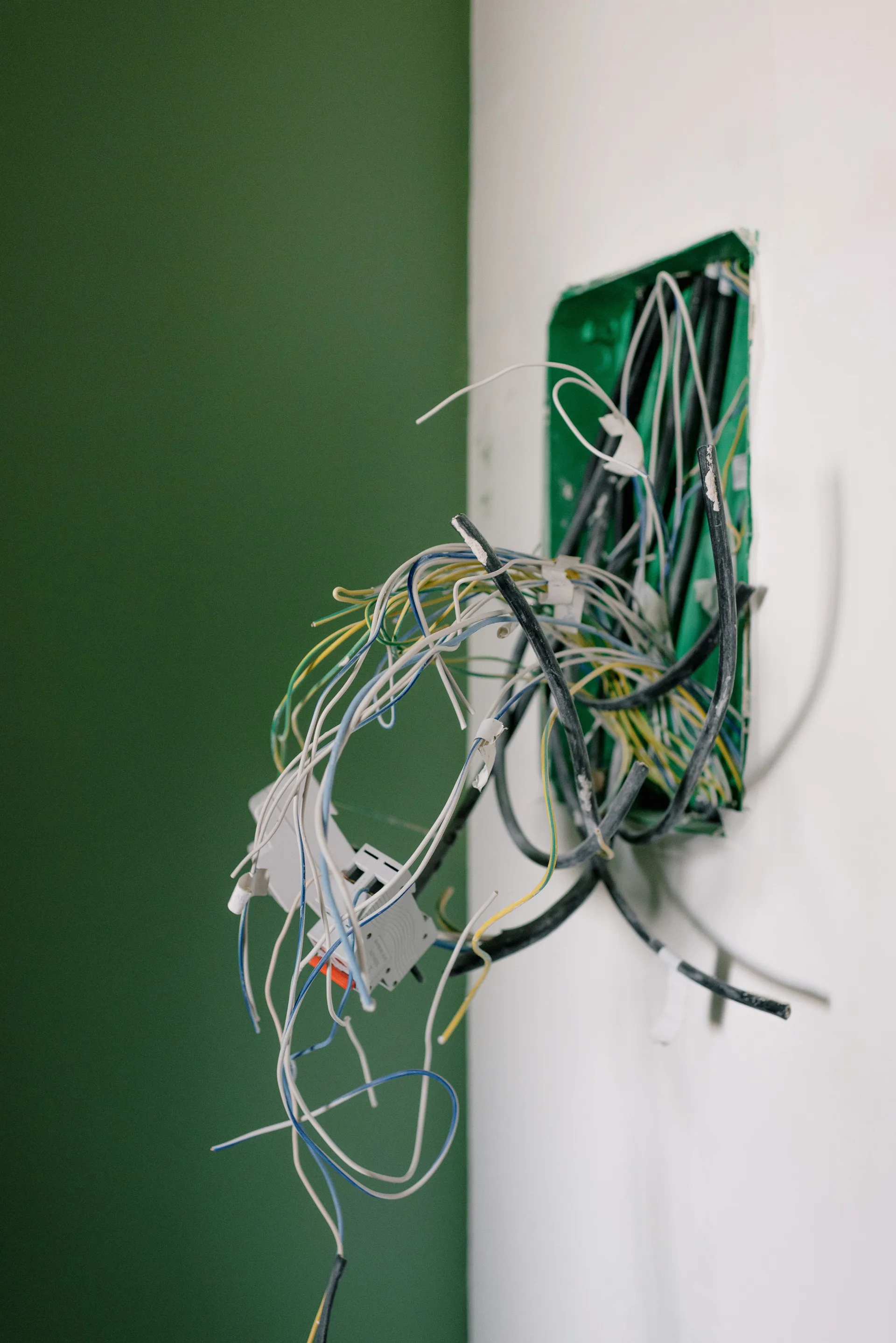 Opened power socket with exposed wires on a white wall