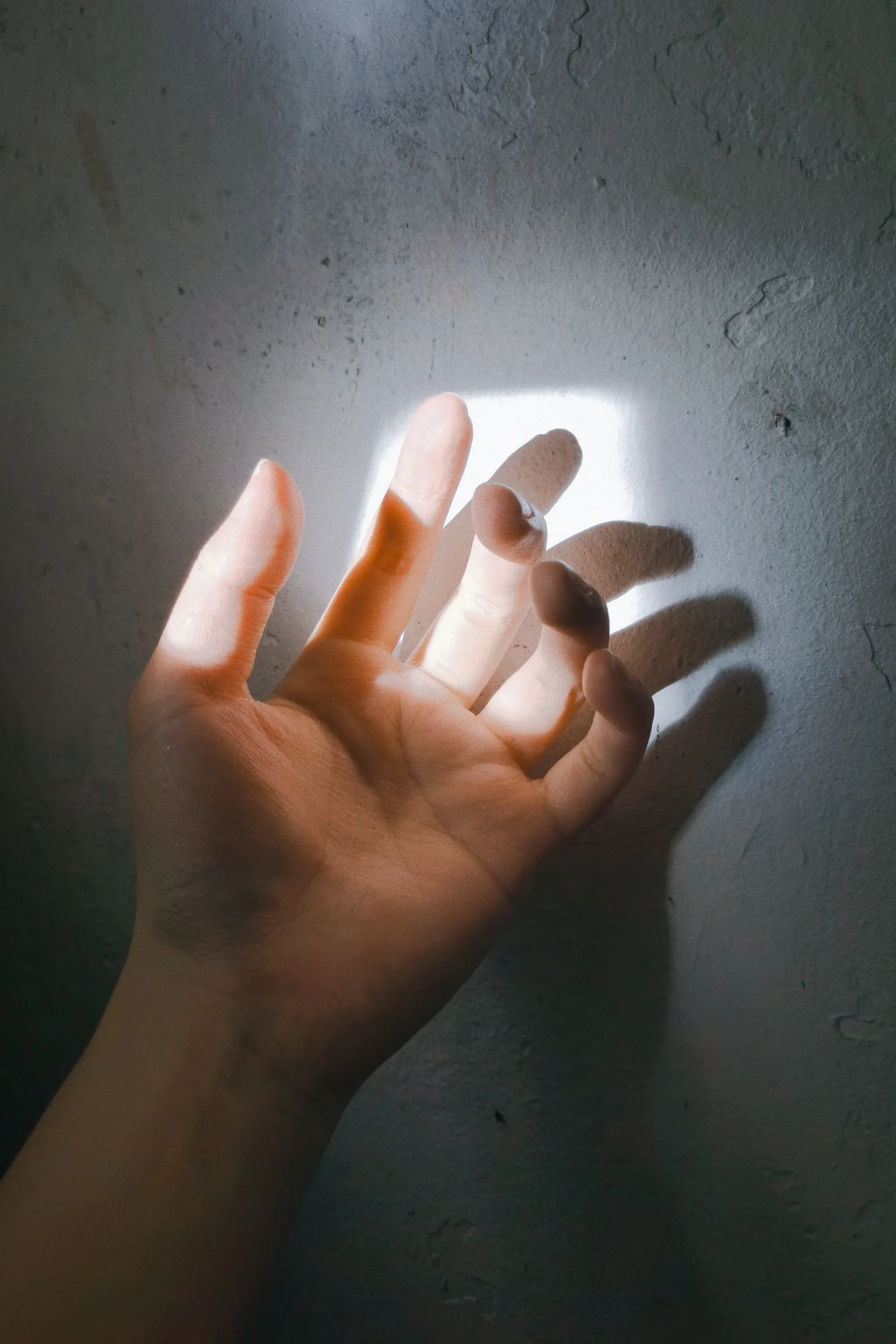 A hand reaching toward light on a wall, casting a shadow