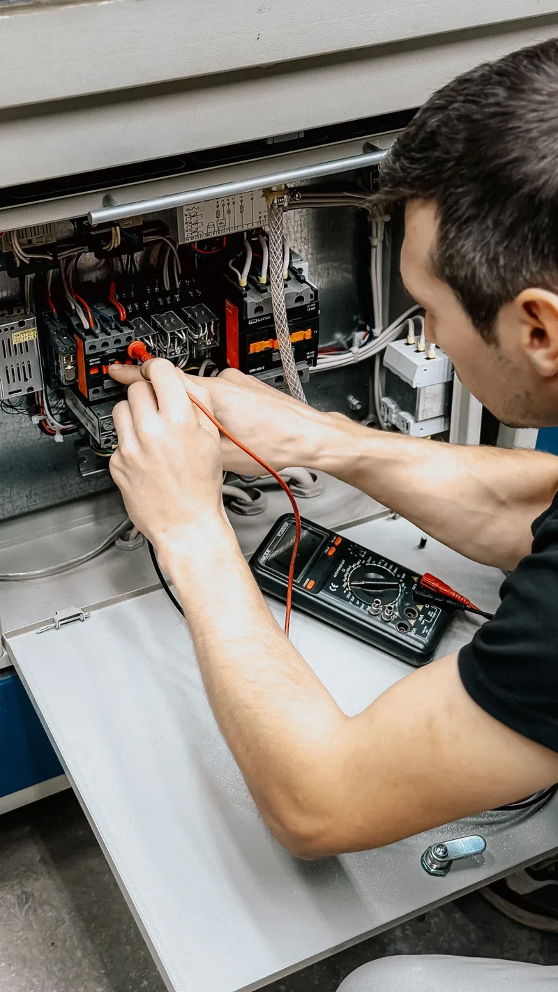 An electrician testing an open breaker panel with a multimeter during a panel assessment