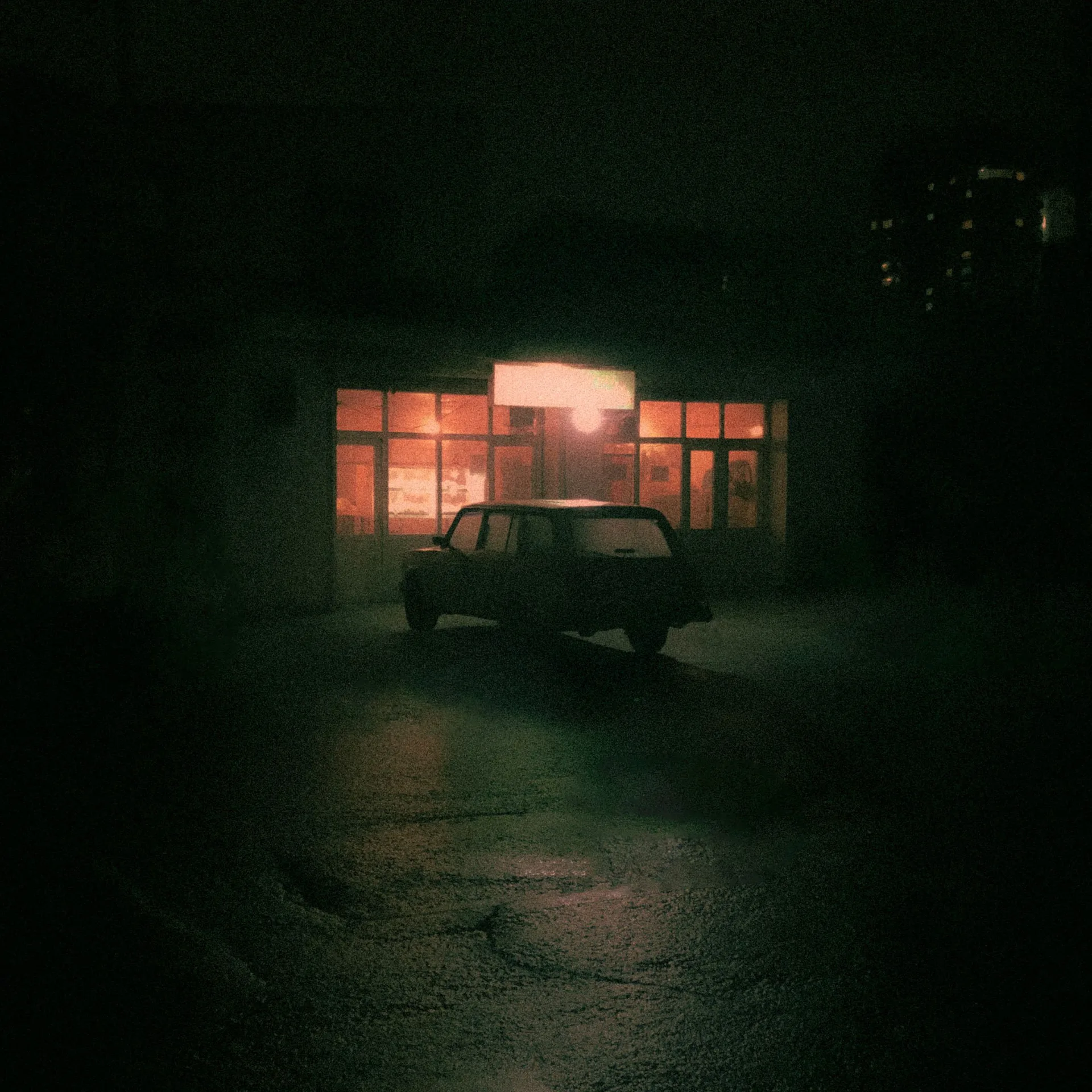 A car in a lit parking area at night beside a bright building