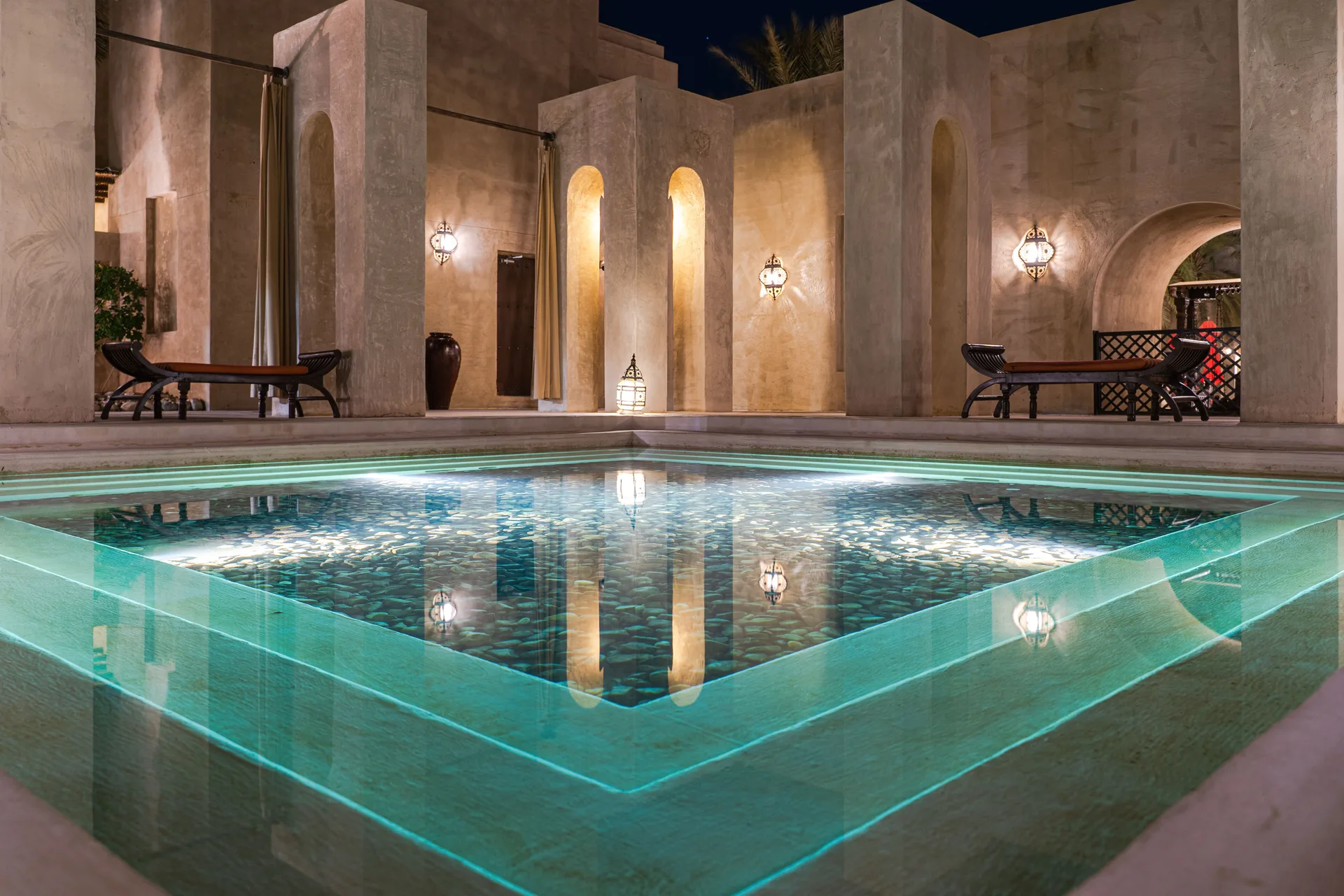 A swimming pool lit up at night beside a hotel building