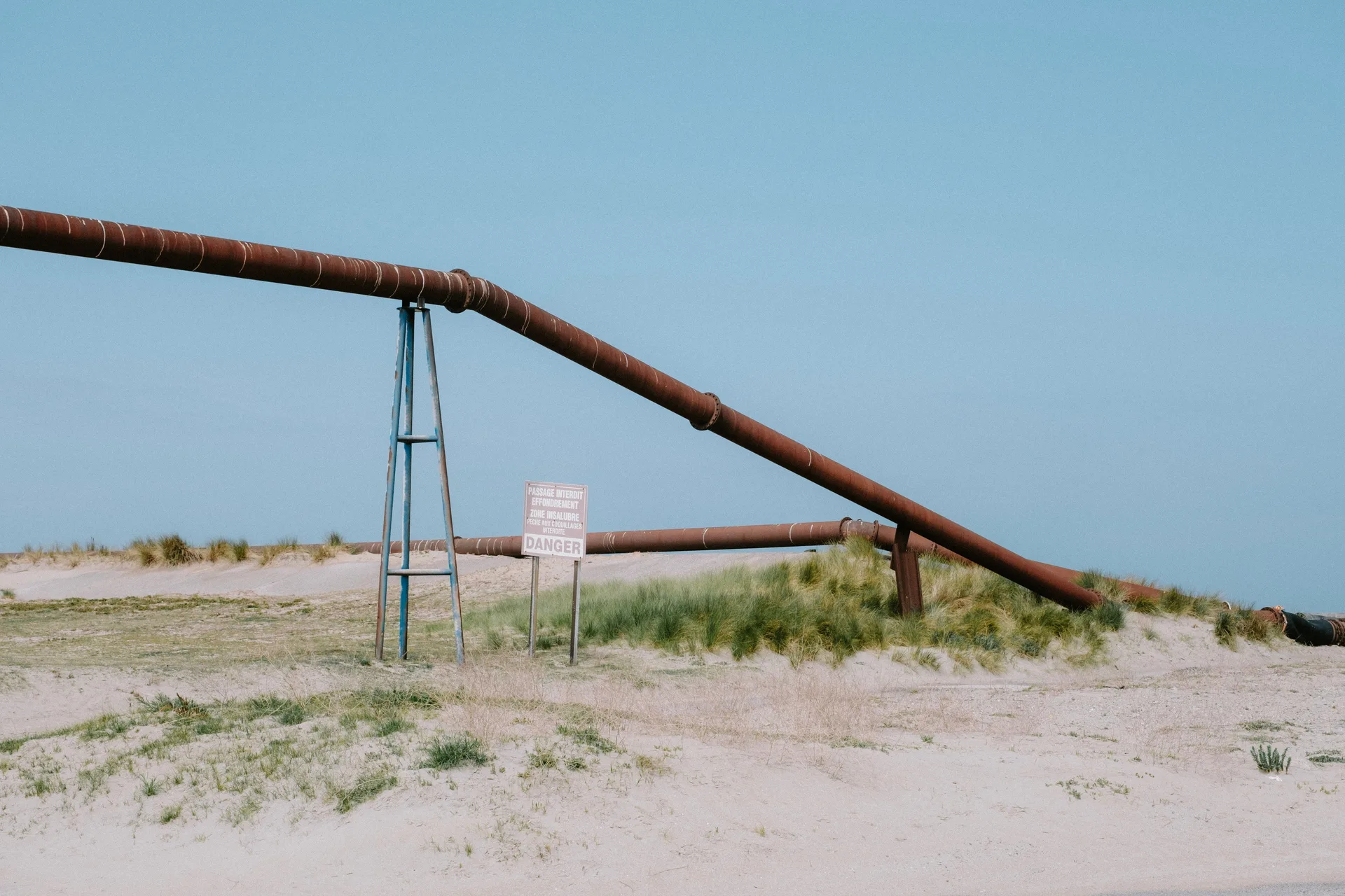 Large rusty industrial pipe over a sandy beach with dune grass