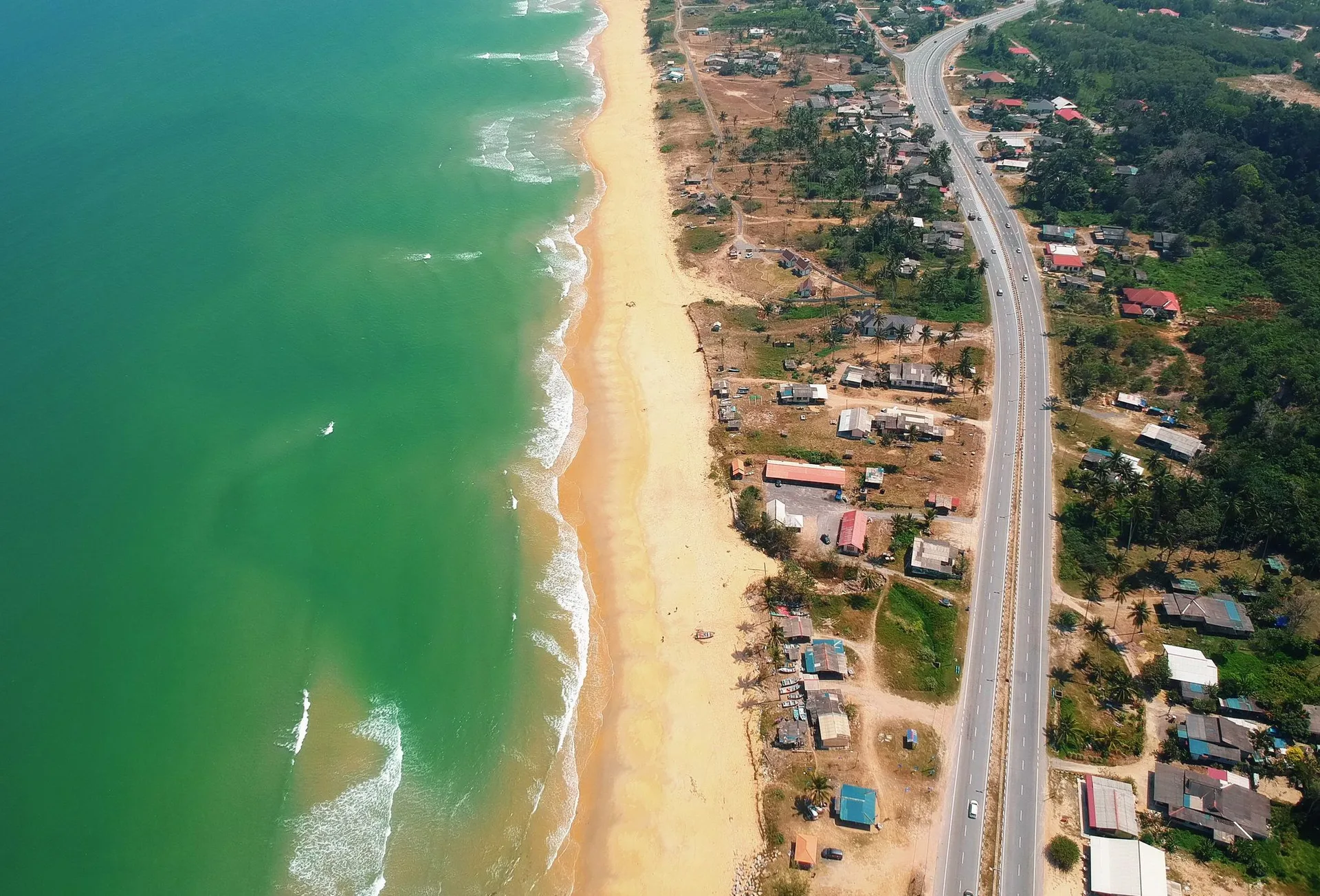 Aerial view of a coastal town with a road running parallel to a sandy beach
