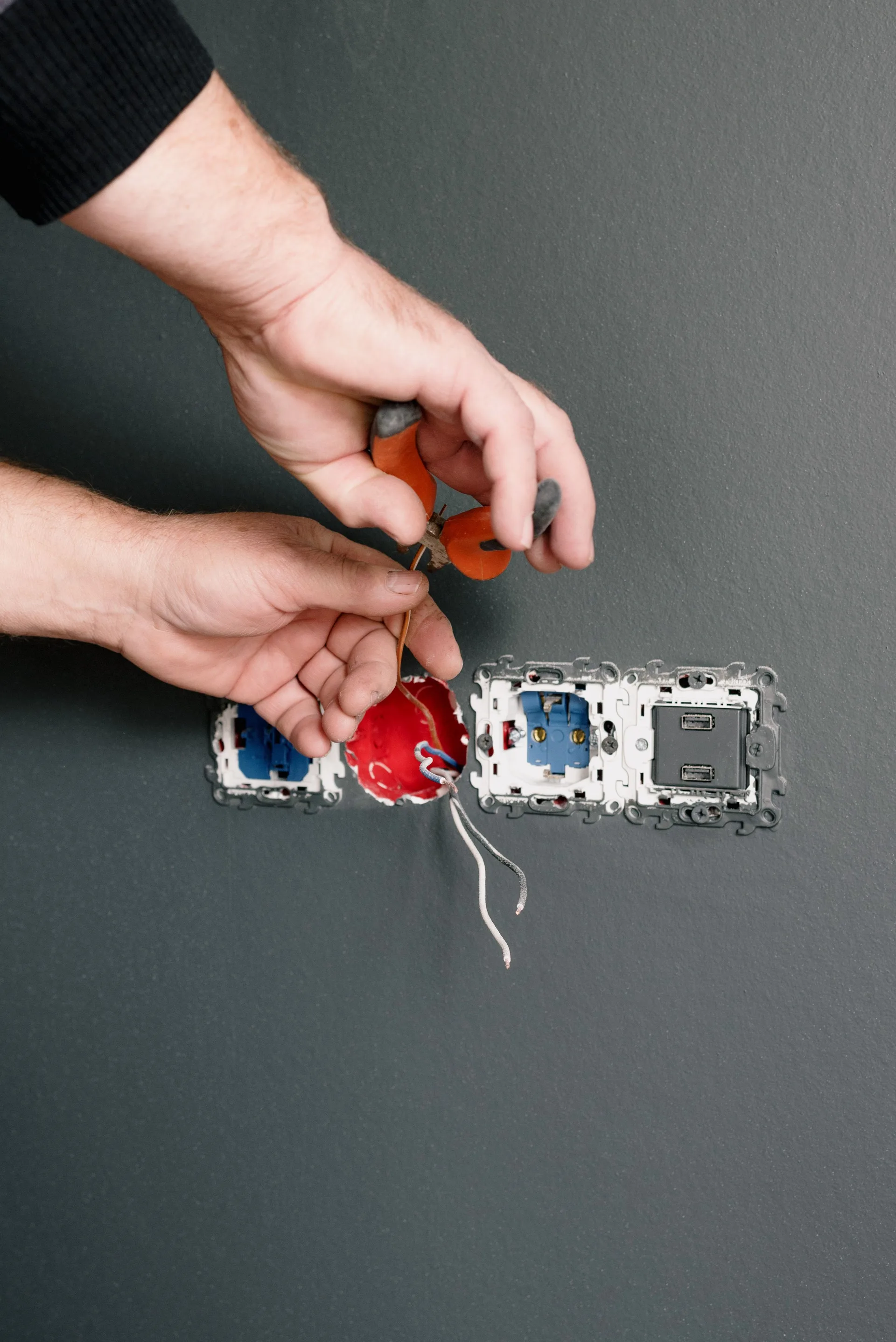 Hands repairing electrical sockets with pliers against a wall